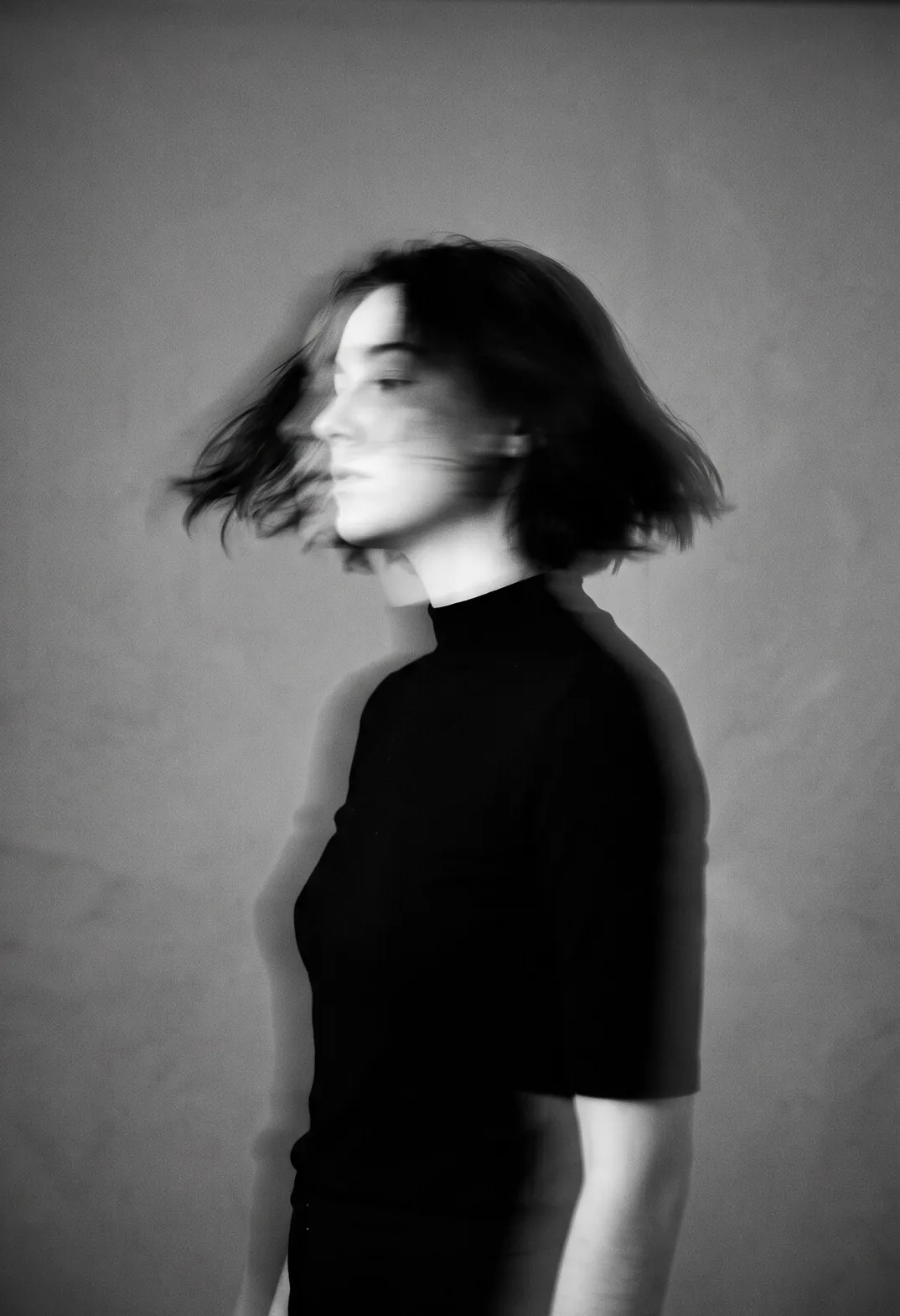Pessoa de preto virando o rosto, em movimento, foto em preto e branco